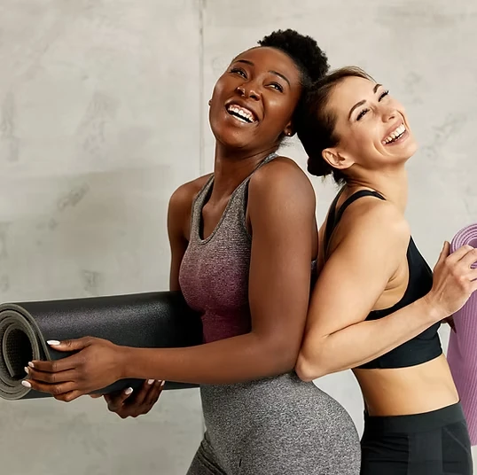 Two students laughing while carrying rolled yoga mats